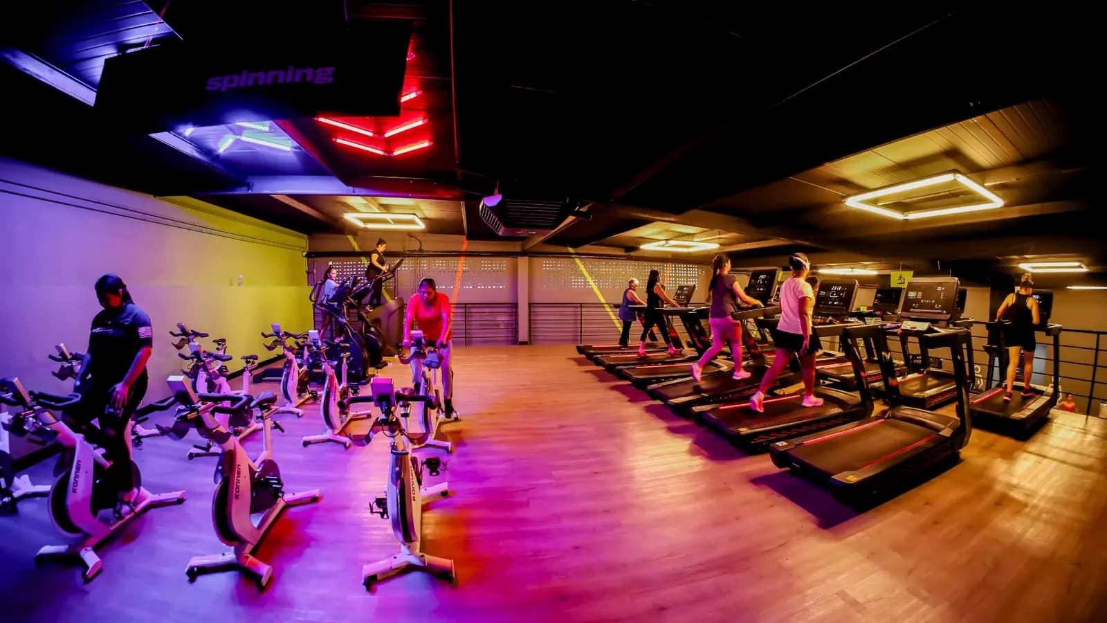 Sala de bike indoor e esteiras da unidade Evoque Heliópolis, com iluminação roxa e laranja