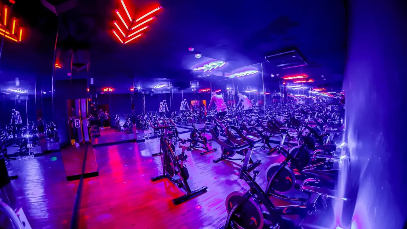 Sala de bike indoor da unidade Evoque Rio Branco, em São Paulo, com luz azul e detalhes em laranja
